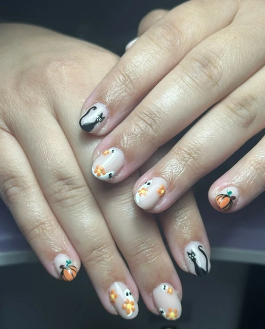 Ongles courts blancs décorés de chats noirs, de citrouilles et de petits fantômes